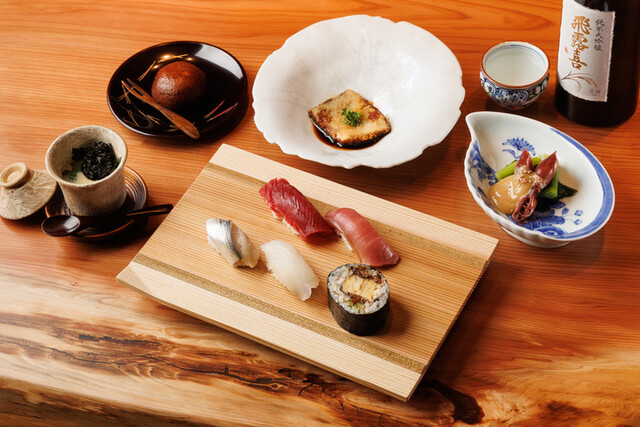 木のテーブルに寿司盛り合わせ、茶碗蒸し、焼き魚、小鉢が並ぶ