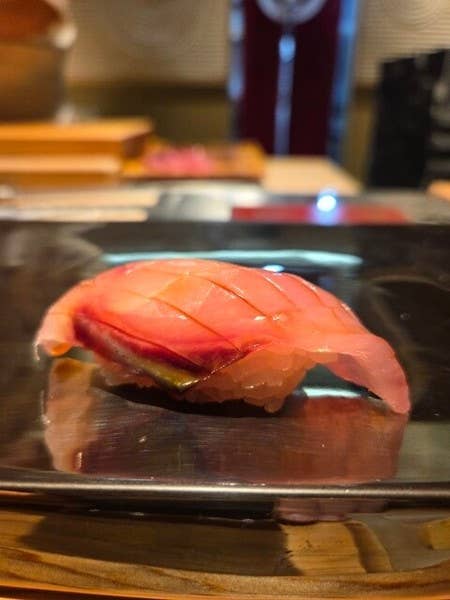 銀色の台に置かれた、包丁の筋が入った赤身の魚の握り寿司の接写