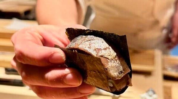 板前の手が焼いた魚の握りを海苔で包んで差し出す接写